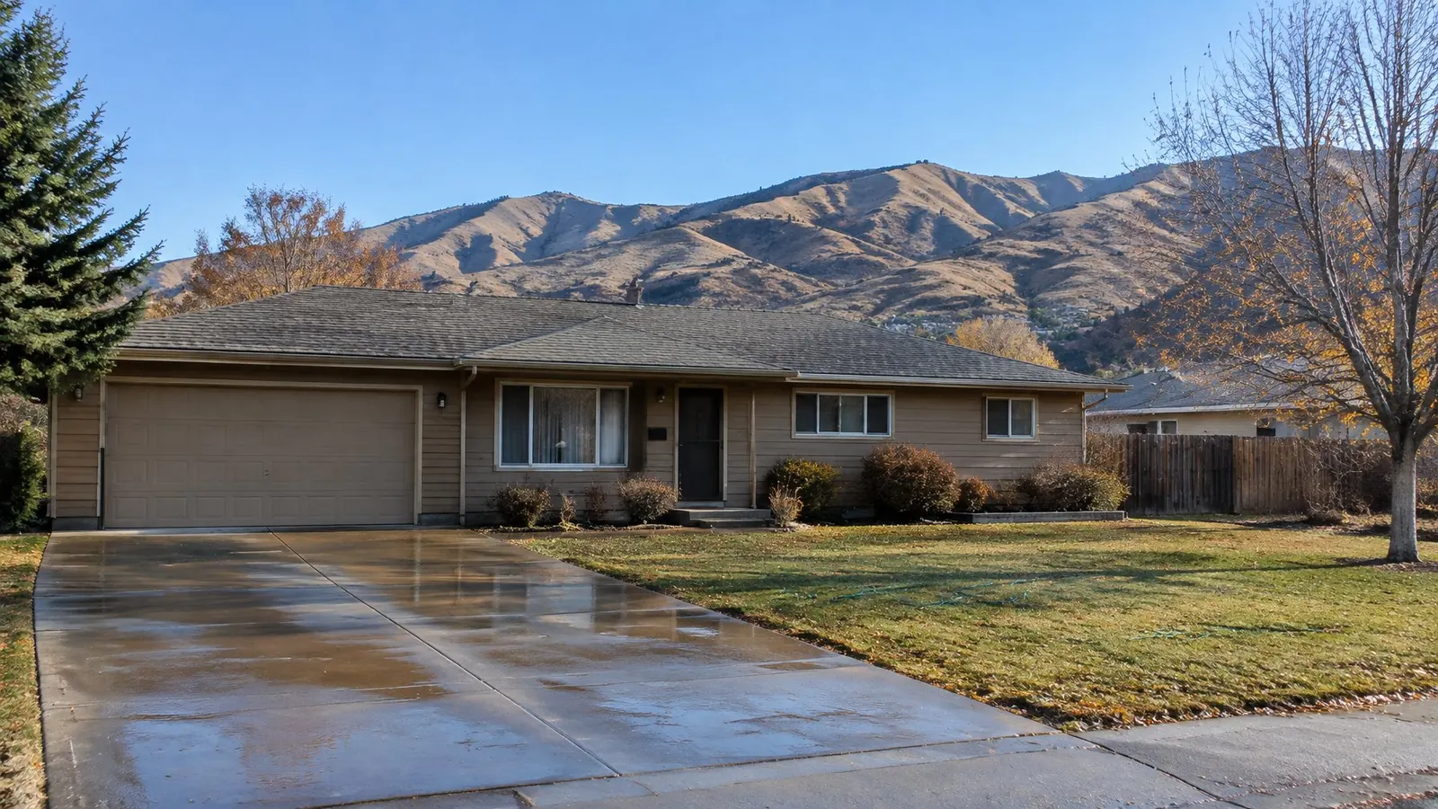 Single-story ranch house with a wet driveway and the Boise foothills behind under a clear sky